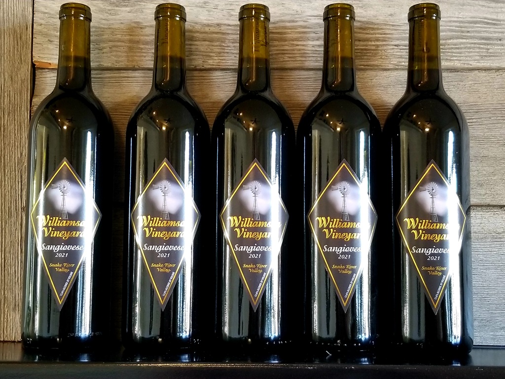 Row of 5 wine bottles of Williamson Vineyards 2021 Sangiovese in front of a weathered grey wood wall